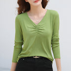 Femme portant un t-shirt vert à manches longues avec col en V et fronces, associée à un pantalon noir. Mode féminine élégante et décontractée.