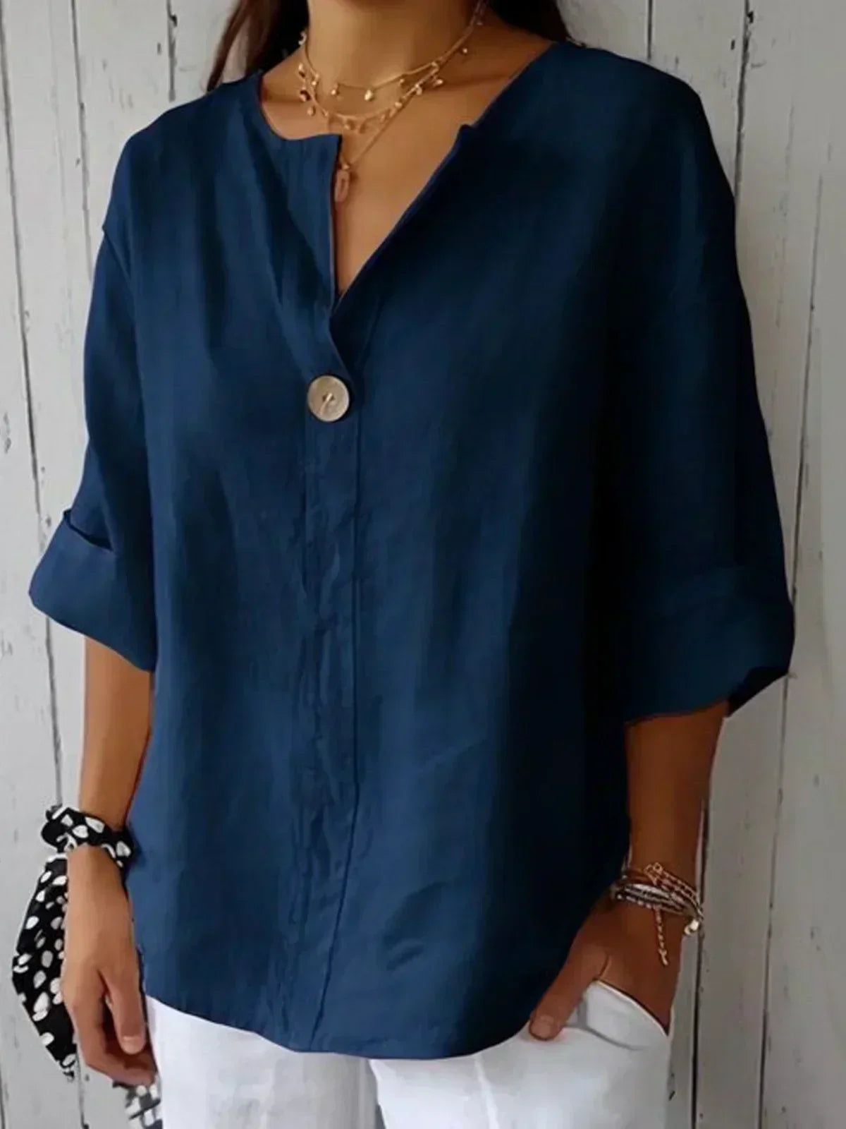 Blouse en lin bleu marine avec bouton unique, manches trois-quarts retroussées, portée par une femme. Mode élégante, tenue décontractée.