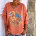 Femme portant un sweat-shirt orange avec un symbole peace and love coloré. Mode décontractée, style bohème, tendance automne.