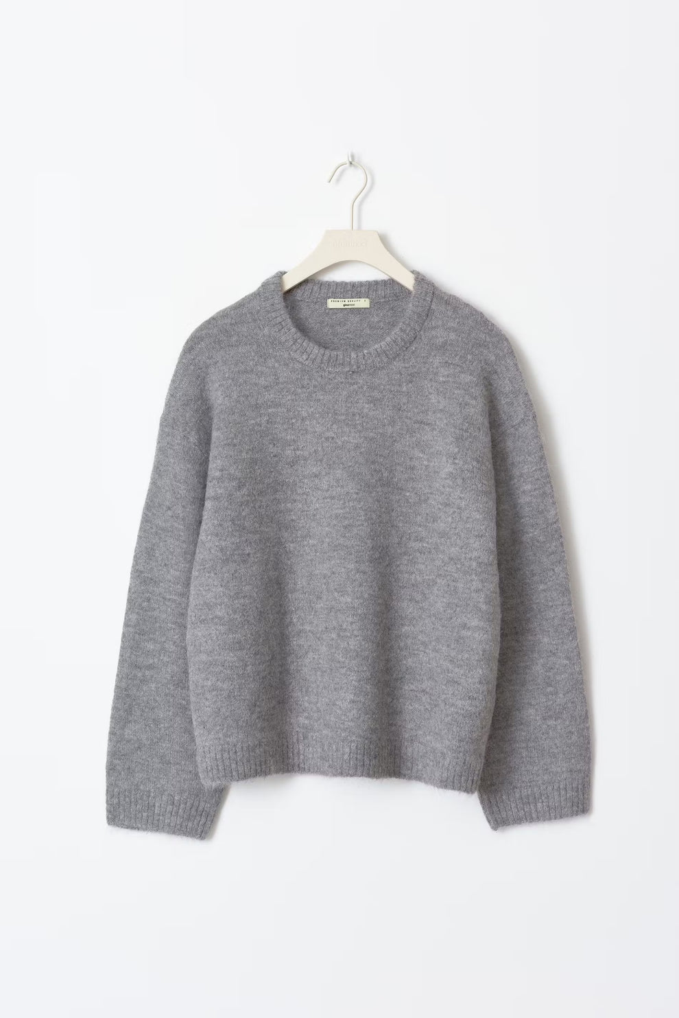 Pull gris en laine, manches longues, col rond, suspendu sur un cintre blanc. Vêtement d'hiver chaud et confortable, style décontracté.