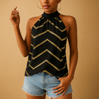 Femme portant un haut noir à motifs dorés en chevrons, avec des boucles d'oreilles créoles et un short en jean. Mode tendance, style chic.