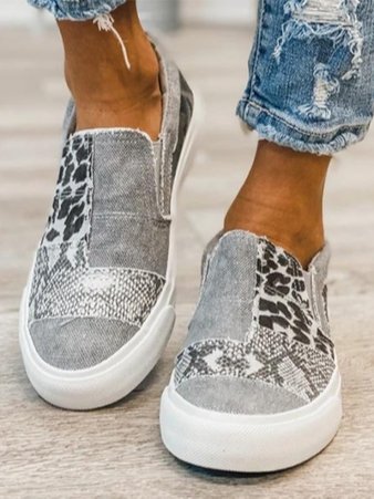 Chaussures slip-on en denim gris avec motifs léopard et serpent, portées avec un jean déchiré. Style décontracté, tendance et moderne.