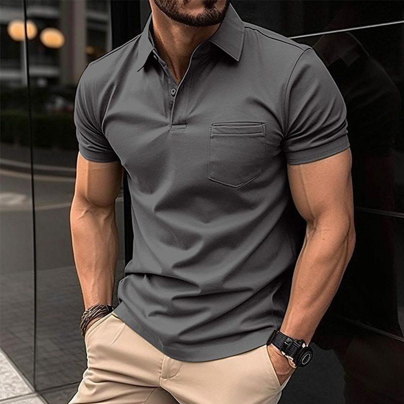 Homme musclé portant un polo gris ajusté, montre noire au poignet, debout en extérieur urbain. Mode masculine, style décontracté élégant.