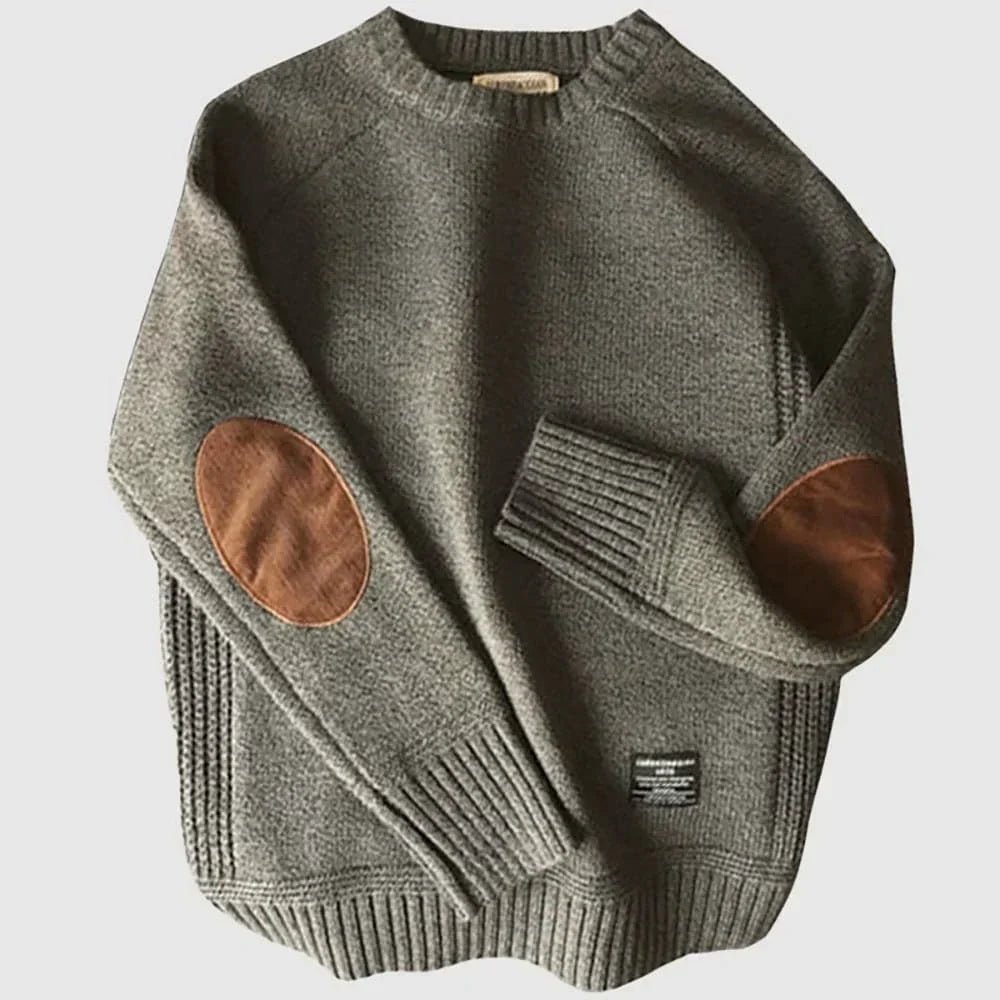 Pull en laine gris avec coudières en cuir marron, manches longues, col rond, style décontracté. Mode automne-hiver, vêtement chaud et élégant.