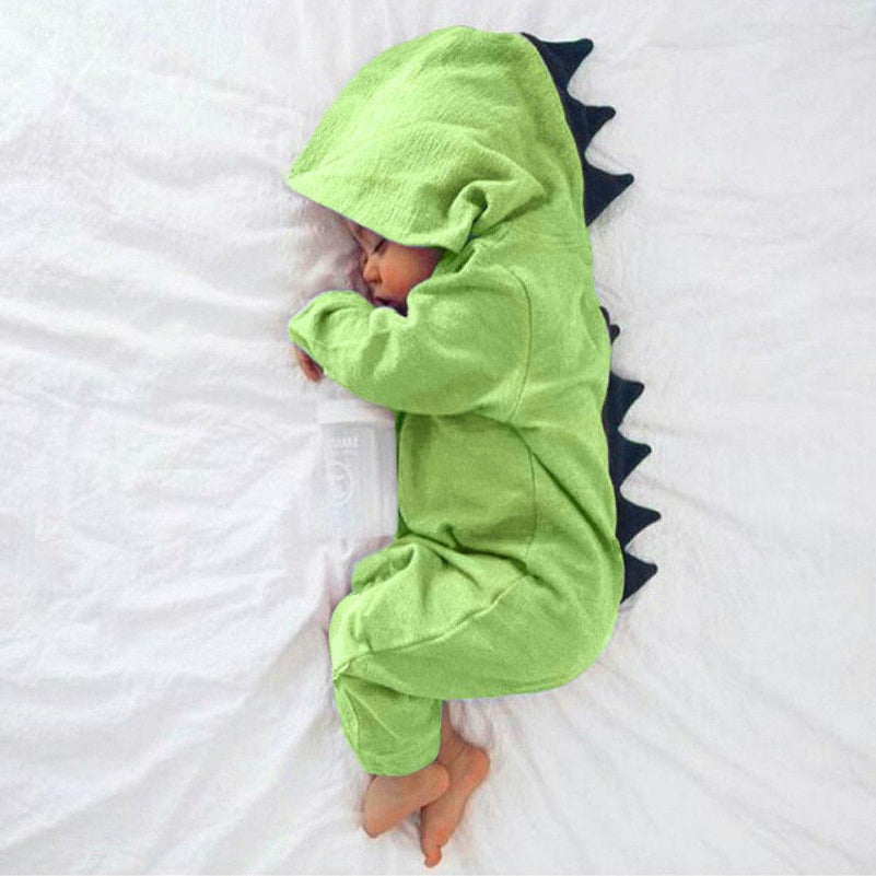 Bébé endormi en pyjama dinosaure vert avec capuche et écailles noires, allongé sur un lit blanc. Tenue mignonne pour enfant, costume dinosaure.