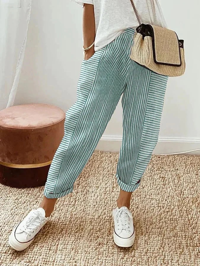Pantalon rayé bleu et blanc, style décontracté, avec un sac en osier et des baskets blanches. Mode estivale tendance pour femmes.