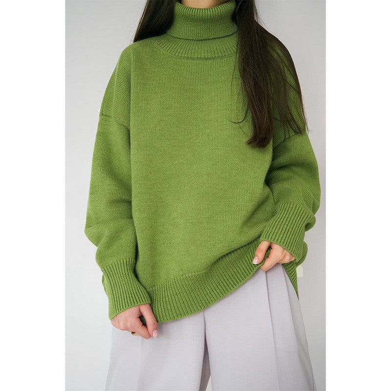 Femme portant un pull vert à col roulé, manches longues, avec un pantalon blanc. Mode automne-hiver, style décontracté et tendance.