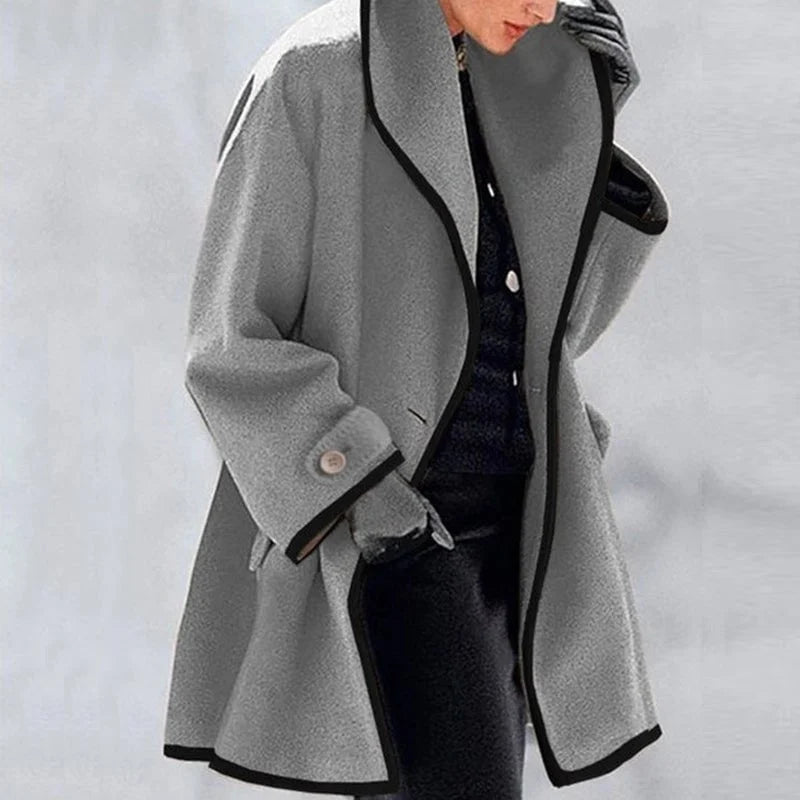 Manteau gris élégant pour femme avec bordure noire, manches larges et bouton décoratif, idéal pour l'hiver. Mode féminine chic et moderne.