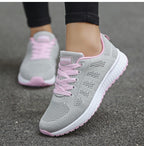 Chaussures de course grises et roses pour femme, semelle blanche, lacets roses, sur fond de trottoir. Confortables et légères, idéales pour le sport.