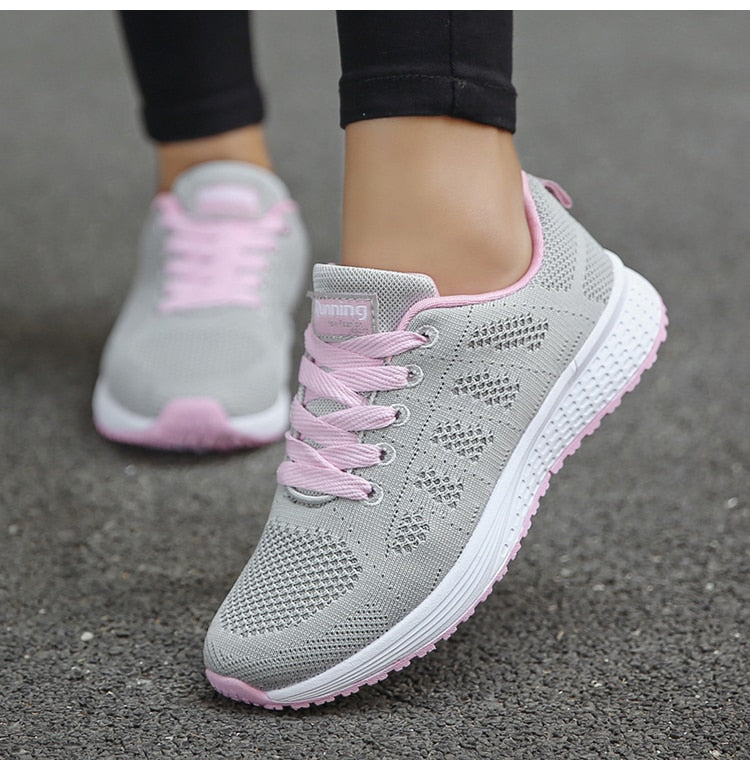 Chaussures de course grises et roses pour femme, semelle blanche, lacets roses, sur fond de trottoir. Confortables et légères, idéales pour le sport.