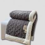 Couverture en laine grise avec motif géométrique, bordée de fausse fourrure blanche, posée sur un lit. Accessoire de literie chaud et élégant.