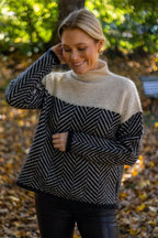 Femme souriante portant un pull à motifs géométriques noir et blanc, col roulé, dans un parc automnal. Mode automne, style décontracté, nature.