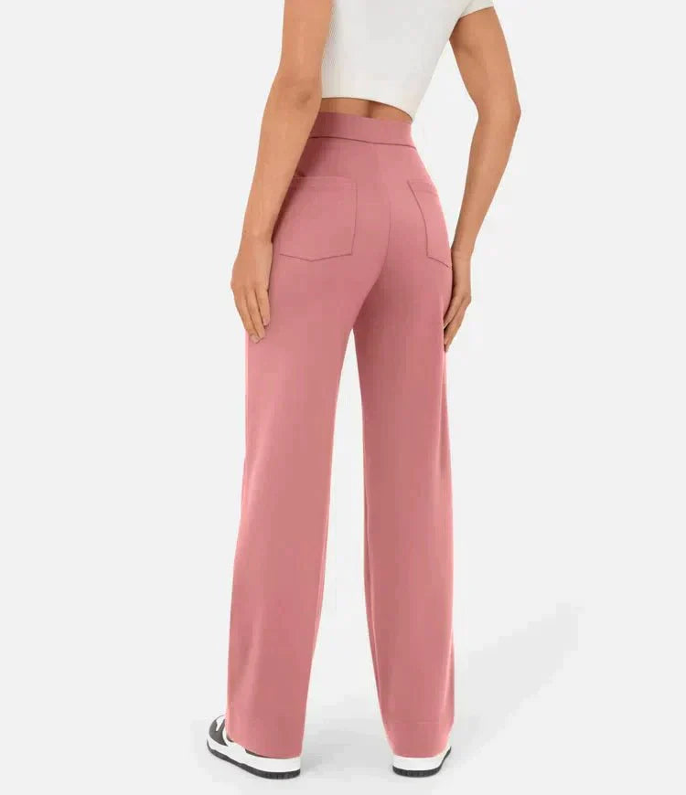 Femme portant un pantalon rose taille haute, coupe large, avec poches arrière, associée à un haut blanc court et des baskets noires et blanches.