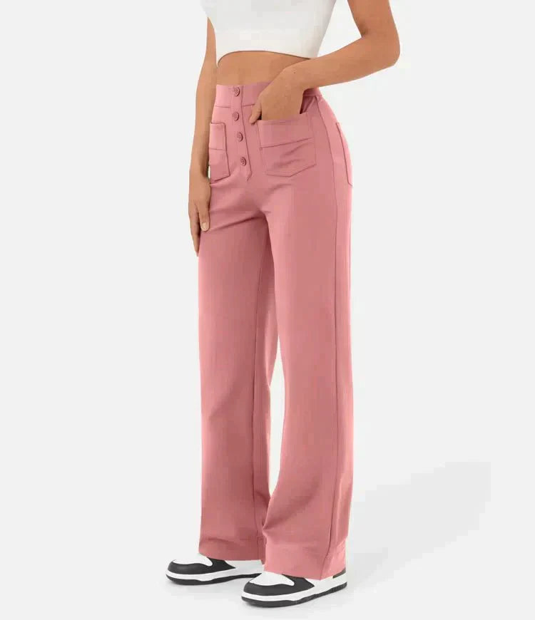 Femme portant un pantalon rose taille haute avec boutons, poches avant, associé à un haut blanc court et des baskets noires et blanches.