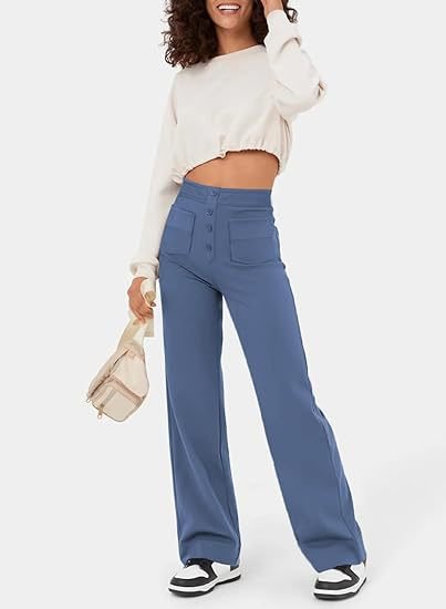 Femme souriante portant un pull court blanc et un pantalon bleu taille haute, tenant un sac beige. Mode décontractée, tendance automne.
