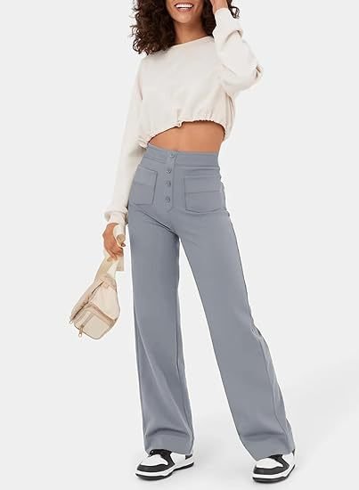 Femme souriante en pull court blanc et pantalon large gris, tenant un sac beige, baskets noires et blanches. Mode décontractée tendance.