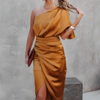 Robe asymétrique en satin doré, élégante et moderne, avec fente latérale. Accessoires minimalistes, ambiance chic et sophistiquée.