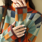 Pull à carreaux multicolores, manches longues, col roulé, motifs orange, bleu et vert, femme avec ongles manucurés, style automne-hiver.