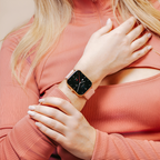 Femme portant une montre connectée rose avec cadran noir, vêtue d'un haut rose. Accessoire mode, technologie portable, style moderne.