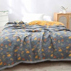 Lit avec couverture à motifs de feuilles jaunes et oranges sur fond gris, chambre lumineuse, commode en bois, décoration moderne et élégante.