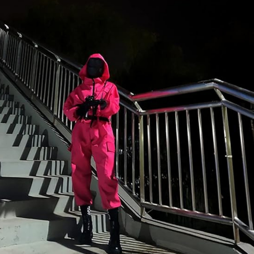 Personne en combinaison rose et masque noir sur un escalier métallique la nuit. Tenue inspirée de série populaire, ambiance mystérieuse.