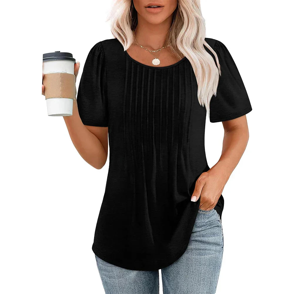 Femme portant un t-shirt noir plissé, tenant un gobelet de café, cheveux blonds ondulés, collier doré, jean décontracté. Mode féminine décontractée.
