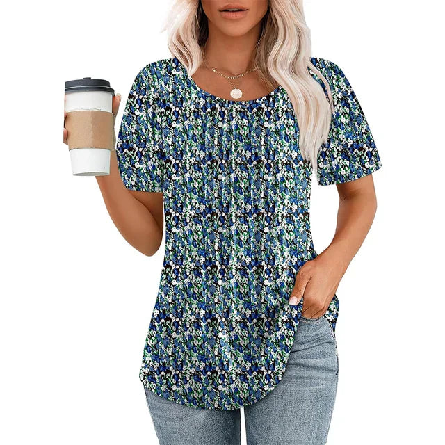 Femme portant un t-shirt à motifs floraux bleus, tenant un gobelet de café, cheveux blonds, collier doré, jeans décontracté. Mode féminine décontractée.