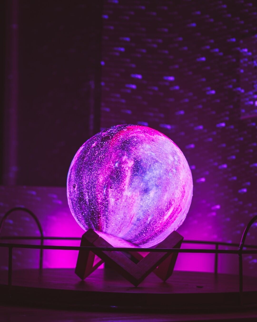 Globe lumineux galaxie violet sur support en bois, éclairé par des lumières LED, créant une ambiance cosmique et futuriste dans une pièce sombre.