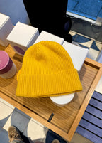 Bonnet jaune en laine posé sur une table en bois, entouré de boîtes blanches. Accessoire de mode hiver, tendance et chaud.