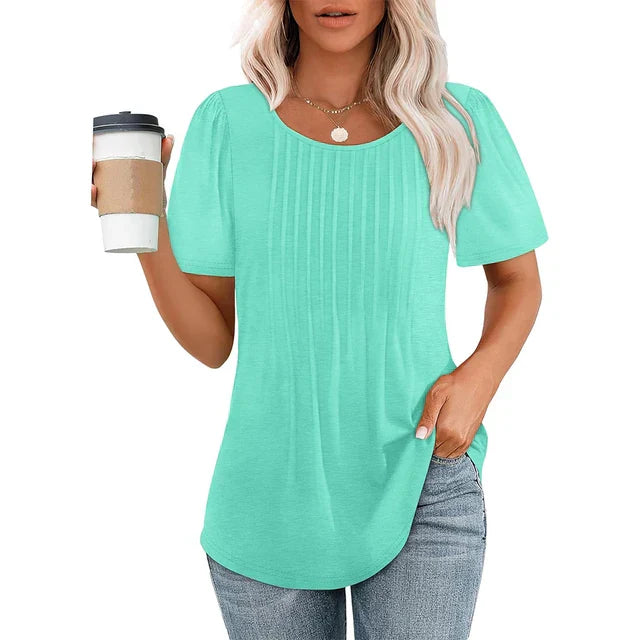Femme portant un t-shirt vert menthe avec manches courtes, tenant un gobelet à café. Mode décontractée, style estival, cheveux blonds ondulés.