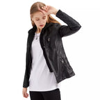 Jeune femme portant un blouson en cuir noir, t-shirt blanc et pantalon noir, posant avec élégance. Mode féminine, style urbain, tendance automne.
