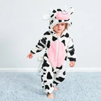 Enfant portant une grenouillère vache, motif noir et blanc, avec capuche à cornes et museau rose, sur tapis bleu. Pyjama animalier mignon.