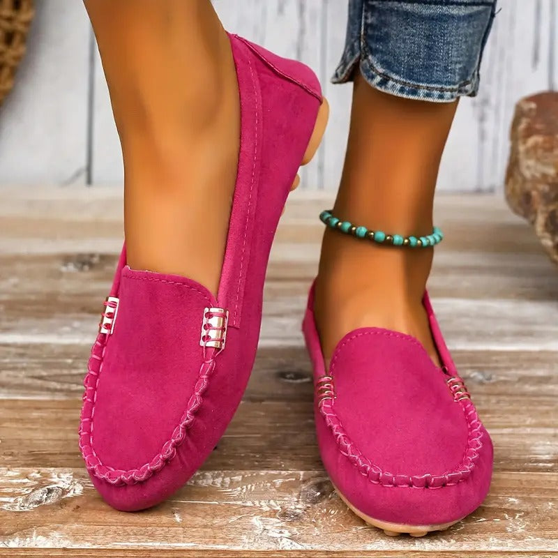 Mocassins roses pour femme en daim, portés avec un jean retroussé et un bracelet de cheville turquoise, posés sur un sol en bois.