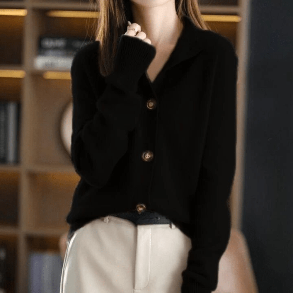 Femme portant un cardigan noir élégant avec boutons, manches longues, sur fond de bibliothèque floue. Mode automne-hiver, style chic et décontracté.