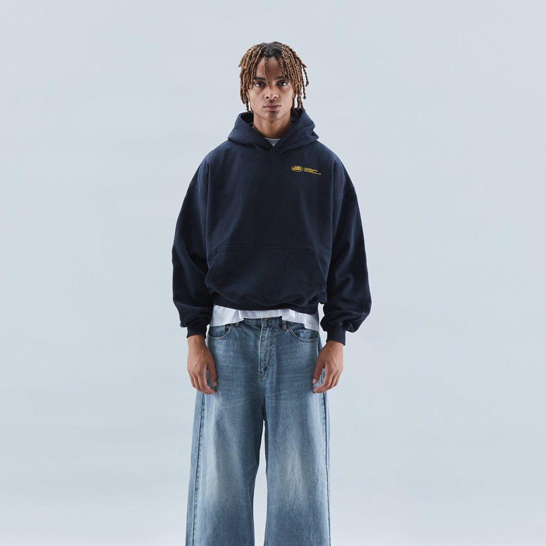 Jeune homme portant un sweat à capuche noir et un jean large, posant sur fond neutre. Mode décontractée, style urbain, vêtements tendance.