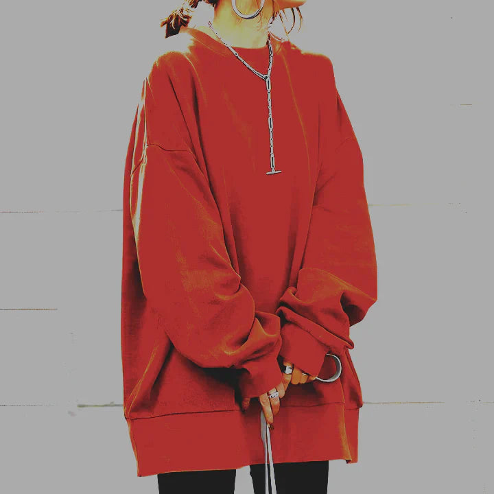 Personne portant un sweat-shirt rouge ample avec un collier argenté, style décontracté, mode urbaine, manches longues, fond gris clair.