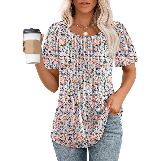 Femme portant un t-shirt à fleurs colorées, tenant un gobelet de café, cheveux blonds ondulés, collier doré, jeans décontracté. Mode féminine décontractée.
