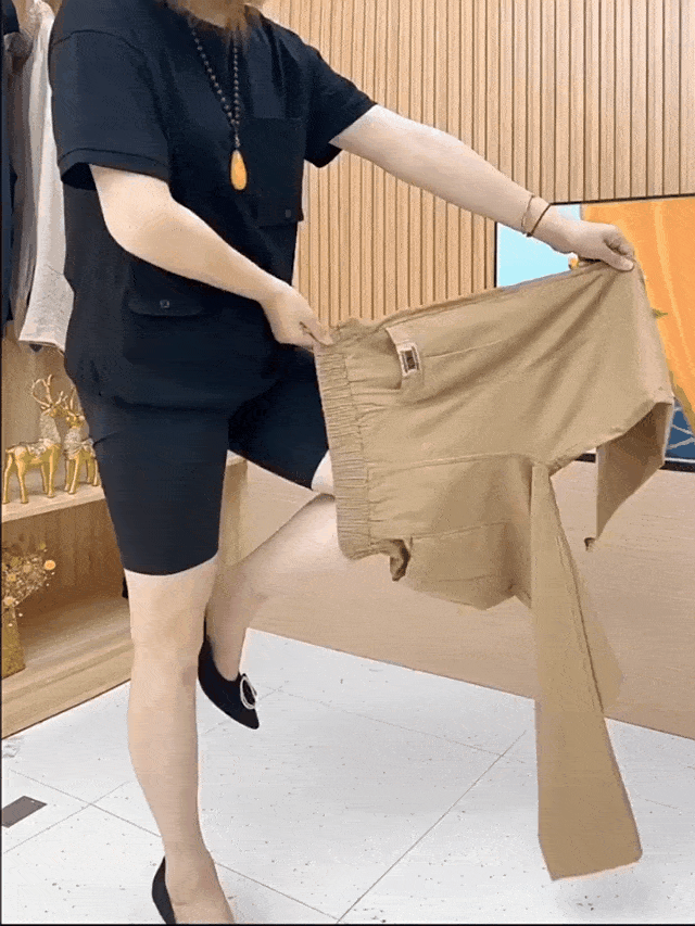 Femme en tenue noire montrant un pantalon beige extensible dans un magasin de vêtements moderne. Mode, vêtements confortables, démonstration produit.