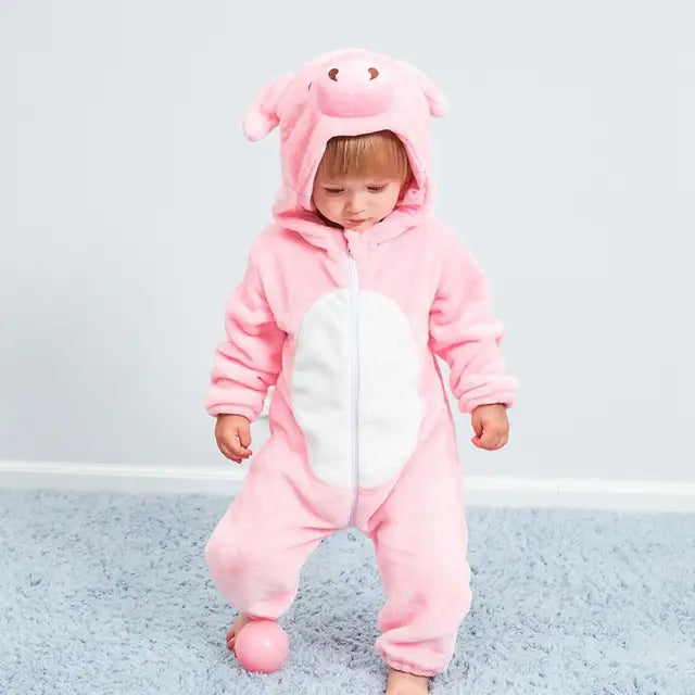 Enfant en grenouillère rose cochon, debout sur tapis bleu avec balle rose. Pyjama animal mignon, tenue bébé confortable, mode enfantine.