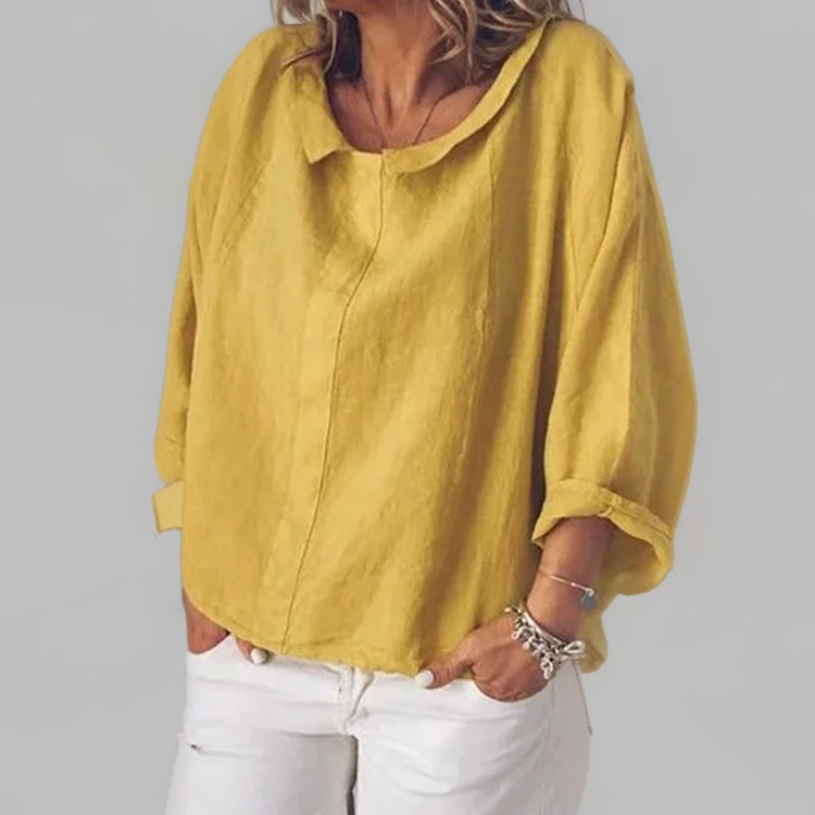 Femme portant une blouse ample jaune en lin, manches retroussées, associée à un pantalon blanc. Mode décontractée, tendance printemps-été.