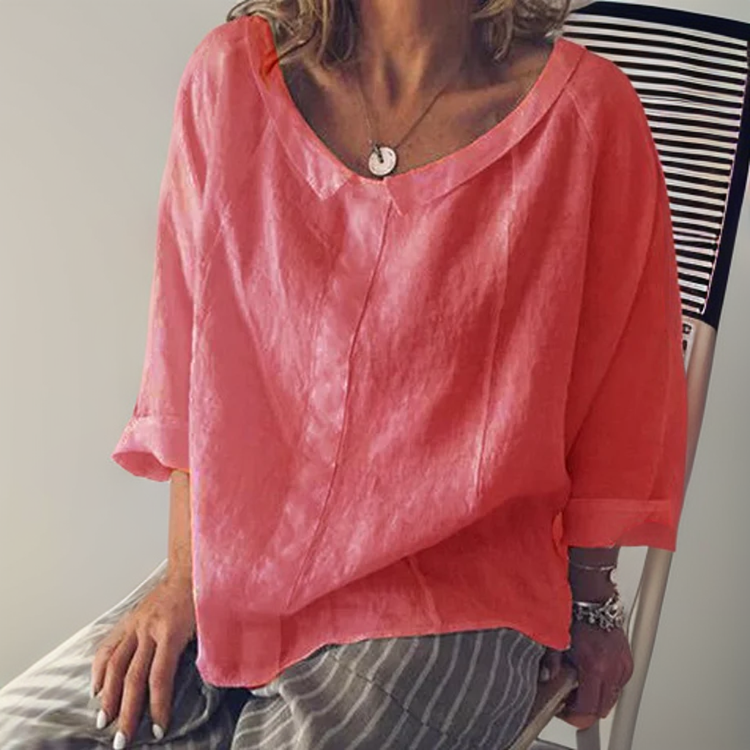 Femme portant une blouse rose ample en lin, manches trois-quarts, assise sur une chaise. Mode décontractée, tendance été, style féminin élégant.