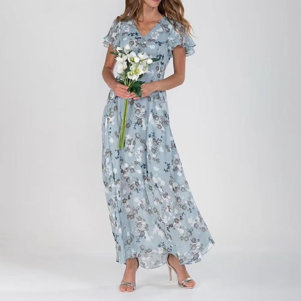 Robe longue fleurie bleue avec manches courtes, portée par une femme tenant un bouquet de fleurs blanches, mode élégante et estivale.