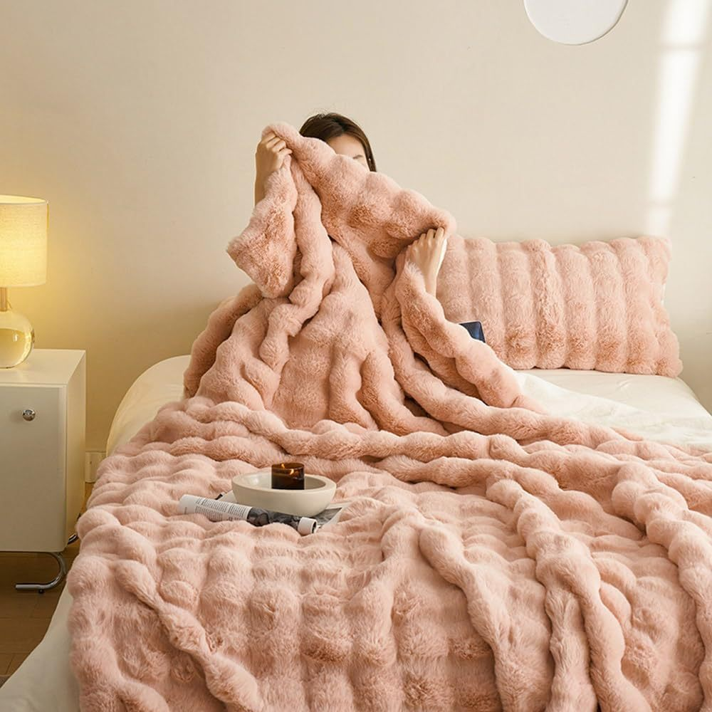 Femme sous couverture en fausse fourrure rose sur lit, lampe allumée, coussin assorti, ambiance cosy. Literie douce et confortable.