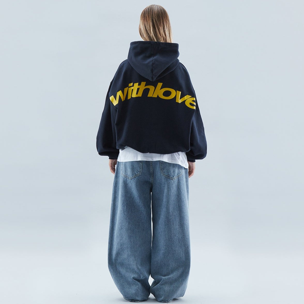 Femme de dos portant un sweat à capuche noir "withlove" et un jean large. Mode urbaine, style décontracté, tendance streetwear.