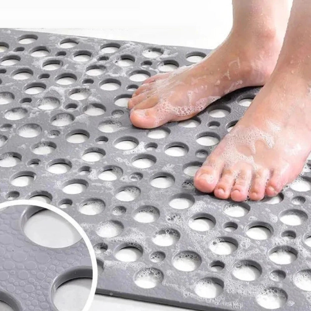 Tapis de bain antidérapant gris avec pieds nus, mousse de savon, surface à trous pour drainage, sécurité douche, salle de bain moderne.