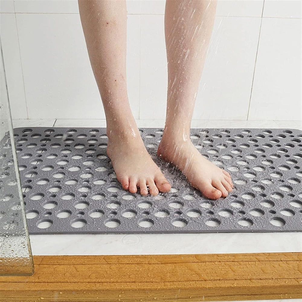 Tapis de douche antidérapant gris avec pieds nus, surface perforée pour drainage efficace, sécurité salle de bain, confort sous la douche.