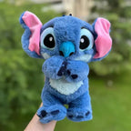 Peluche Stitch bleue avec grandes oreilles roses, tenue dans une main, sur fond de verdure. Jouet Disney mignon, idéal pour enfants et collectionneurs.
