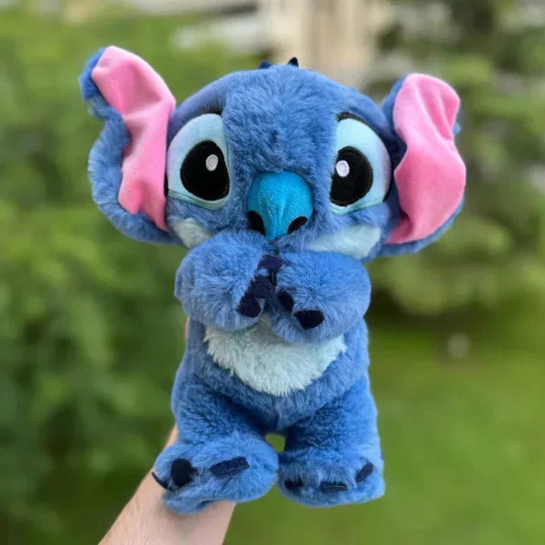 Peluche Stitch bleue avec grandes oreilles roses, tenue dans une main, sur fond de verdure. Jouet Disney mignon, idéal pour enfants et collectionneurs.