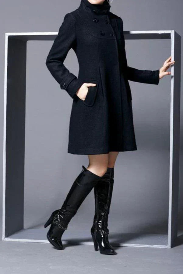 Manteau noir élégant pour femme, coupe ajustée, avec poches, porté avec des bottes en cuir noir à talons hauts. Mode automne-hiver chic.