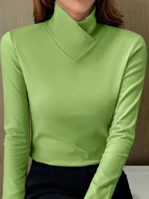 Femme portant un pull vert à col roulé asymétrique, manches longues, sur fond neutre. Mode élégante, tendance automne-hiver.